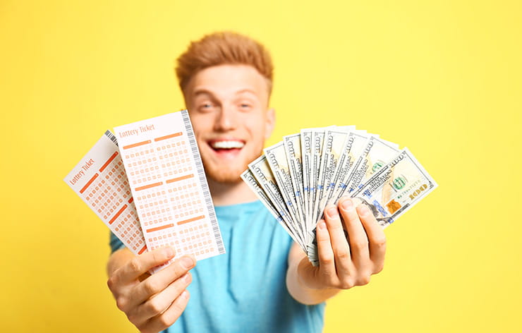 A man holding up lottery tickets and a cash prize